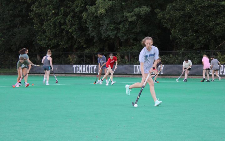 Ellery Duval runs on a field with a field hockey stick