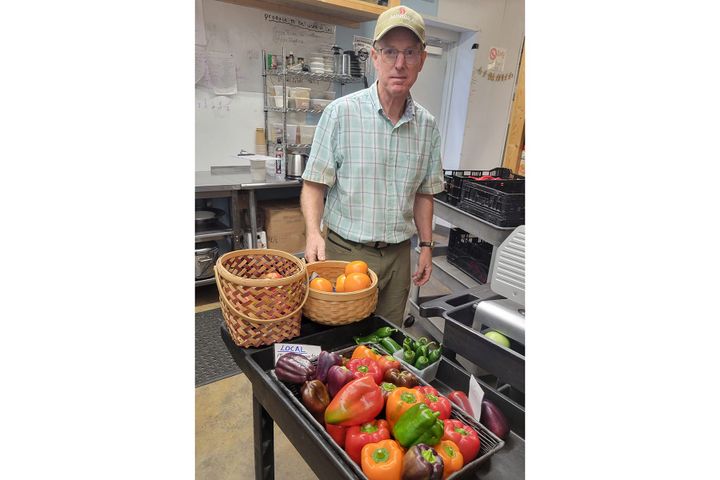 Craig Harkrider stands in a kitchen behind a cart full of green, red, orange and purple peppers
