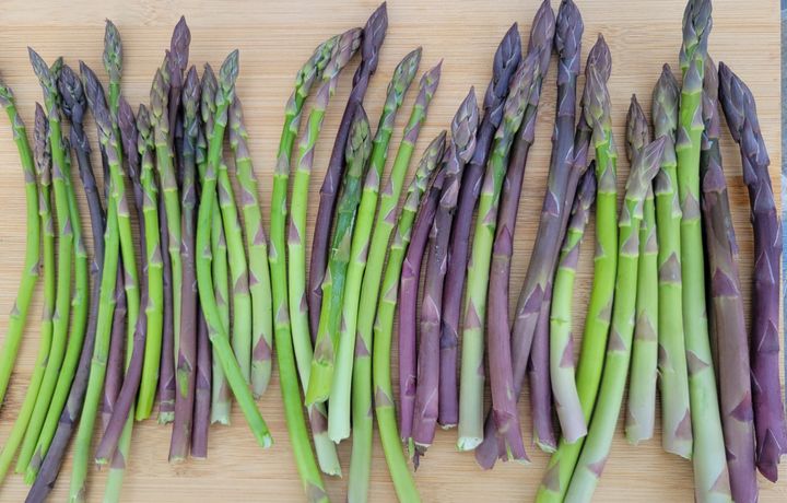 Purple and green asparagus stocks laid out on a cutting board