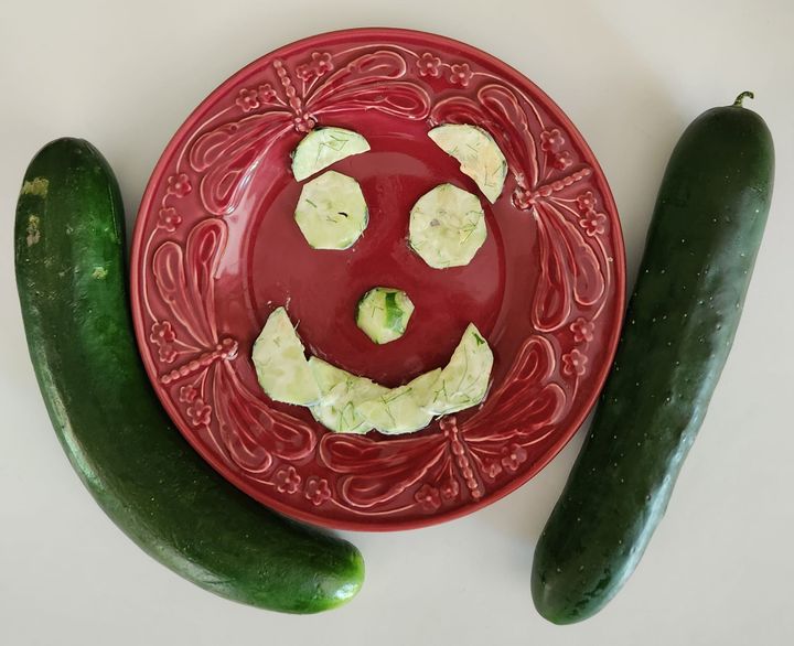 A plate of sliced cucumbers arranged in a smiley face, moisten with crème fraiche and topped with dill