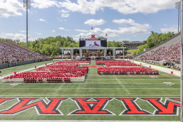 Nearly 4,800 Miami University students wearing red gowns sit in rows on Miami's football field at Yager Stadium