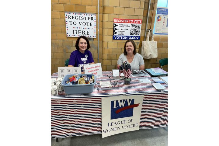 Two women sit behind a LWV table