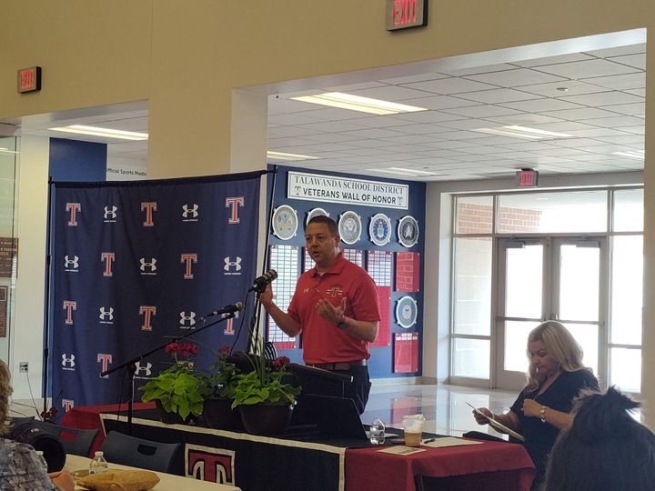 Wes Cole stands at a microphone near a Talawanda backdrop