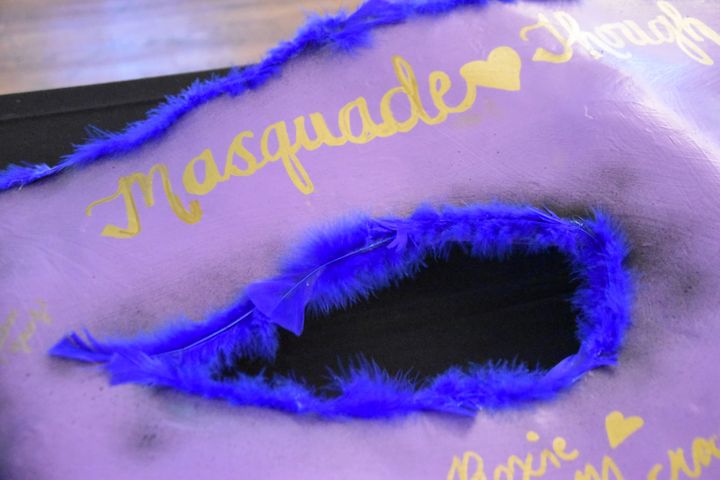 A purple masquerade mask with blue feathers