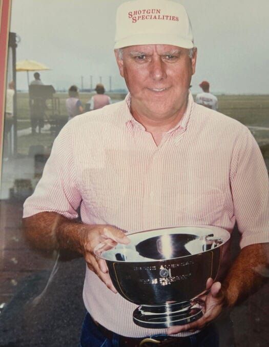 David Albert Wolk wearing a red and white stripped button up shirt and a white hat that reads "Shotgun Specialities" in red font.