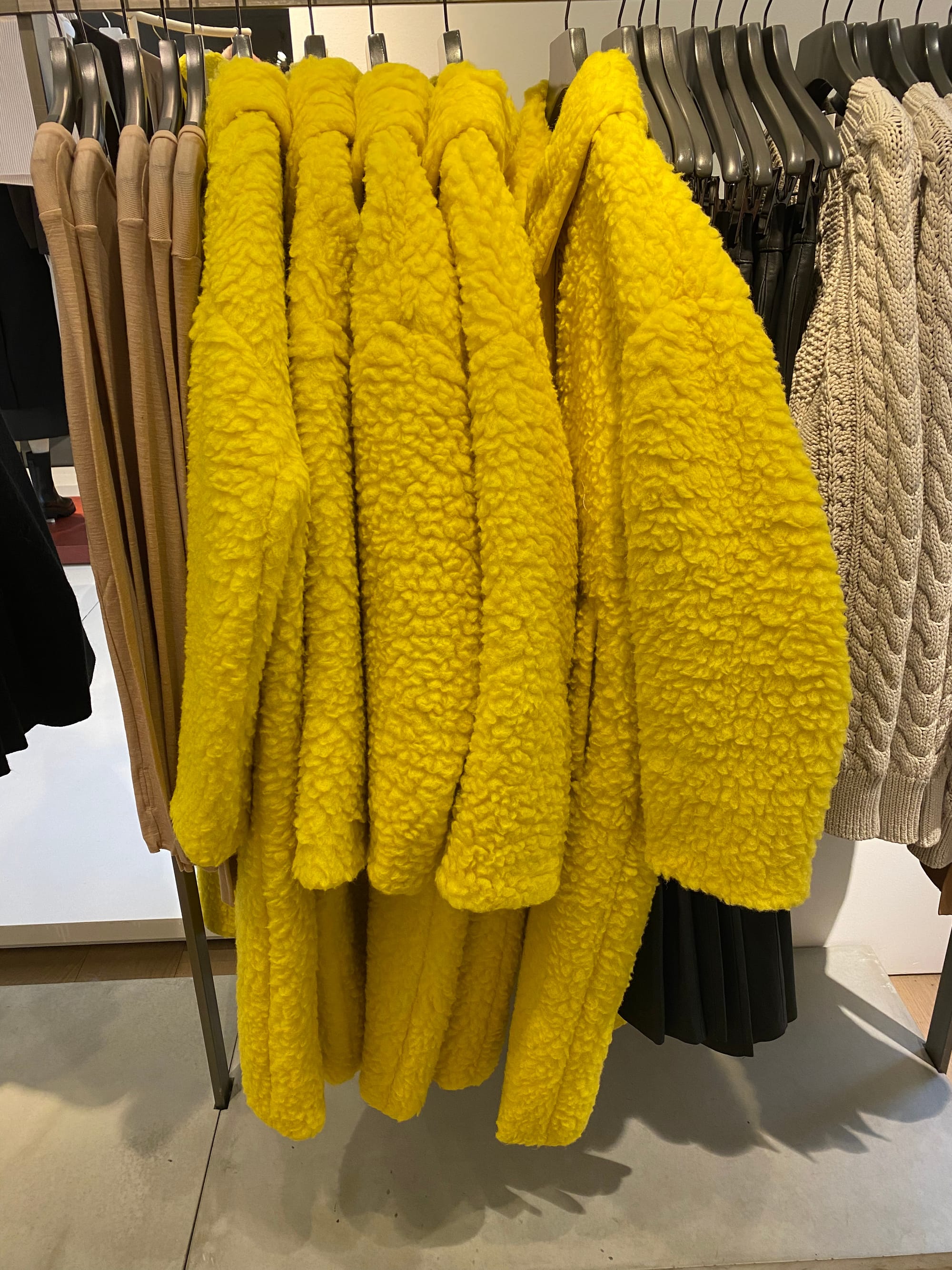 Five shaggy overcoats in bright yellow on a clothing rack at Cos.