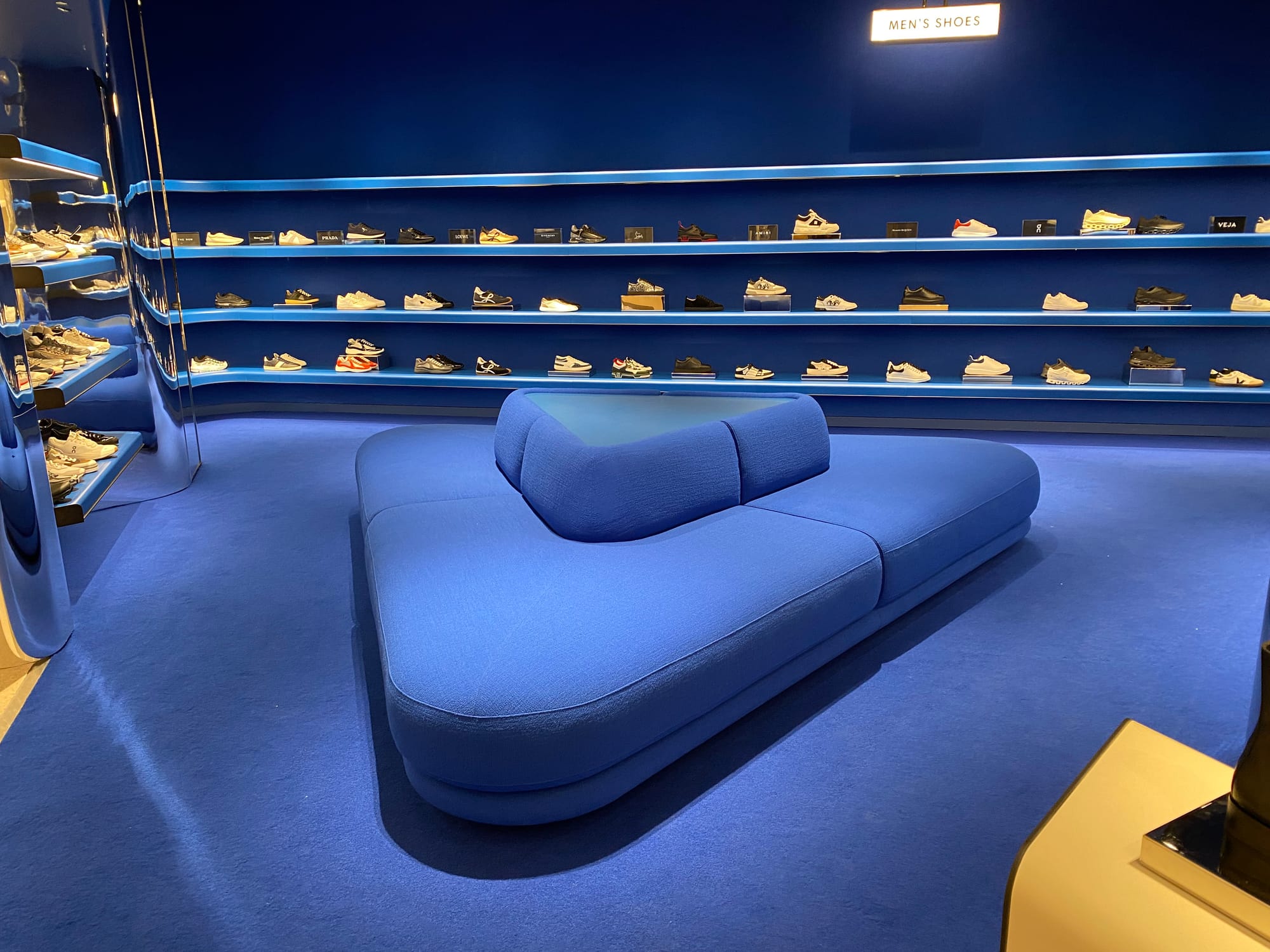 Men's Shoes department at Holt Renfrew with blue carpet, seating, and walls.