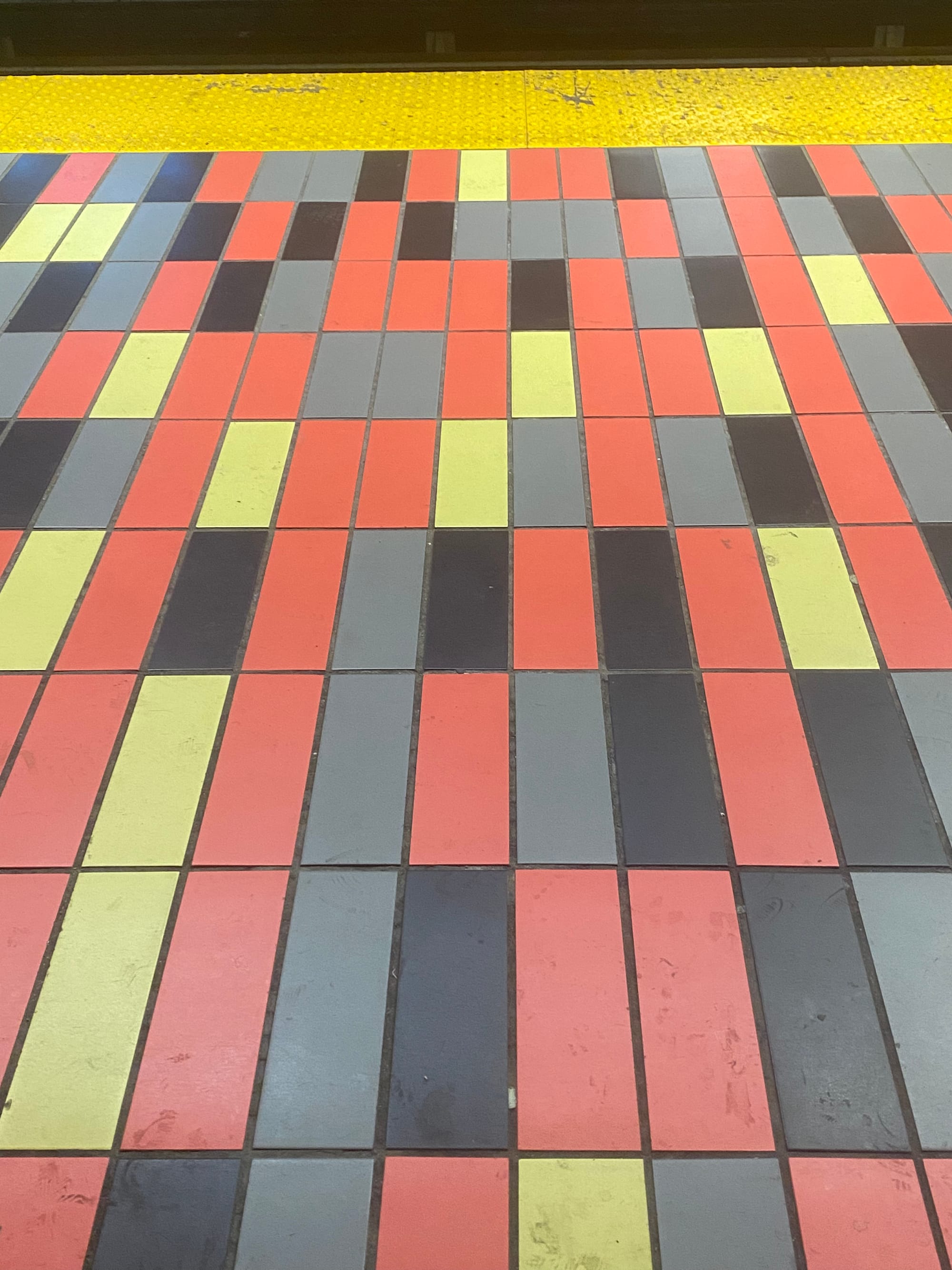 Métro platform with red, yellow, grey, and black tiles in an irregular pattern.
