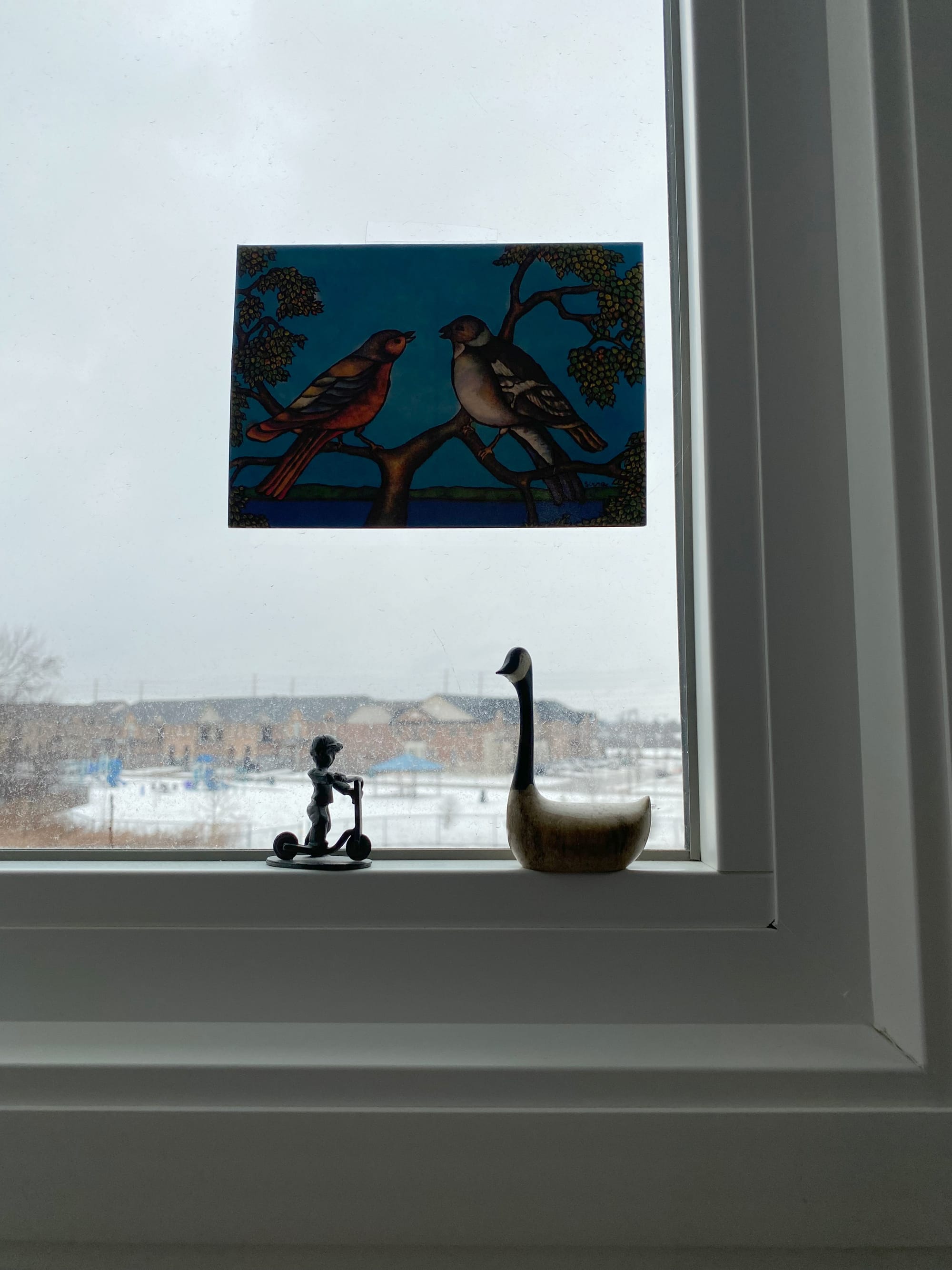 Windowsill with two figurines _ a boy on a scooter and a Canada Goose – as well as a greeting card attached to the window pane.