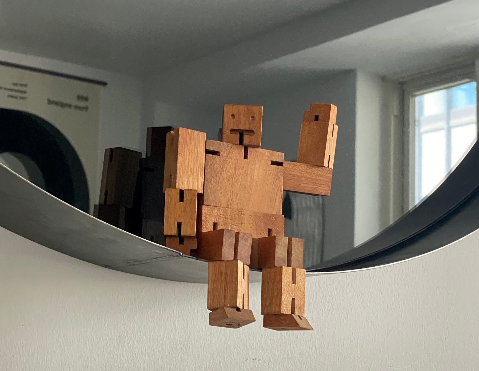 Wooden robot figurine resting on the rim of a smoked glass mirror.
