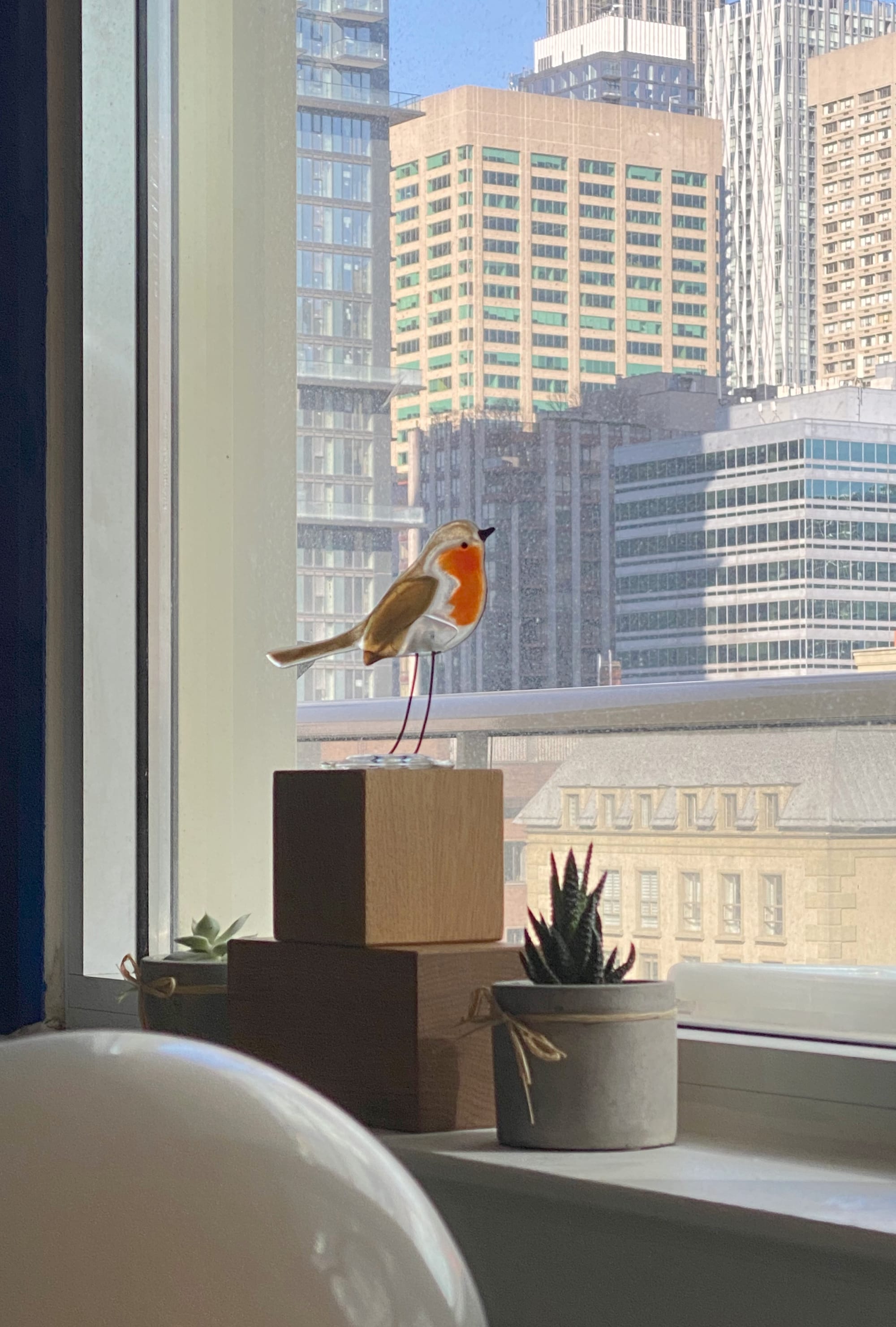 Windowsill vignette with stacked wooden blocks supporting a glass robin.