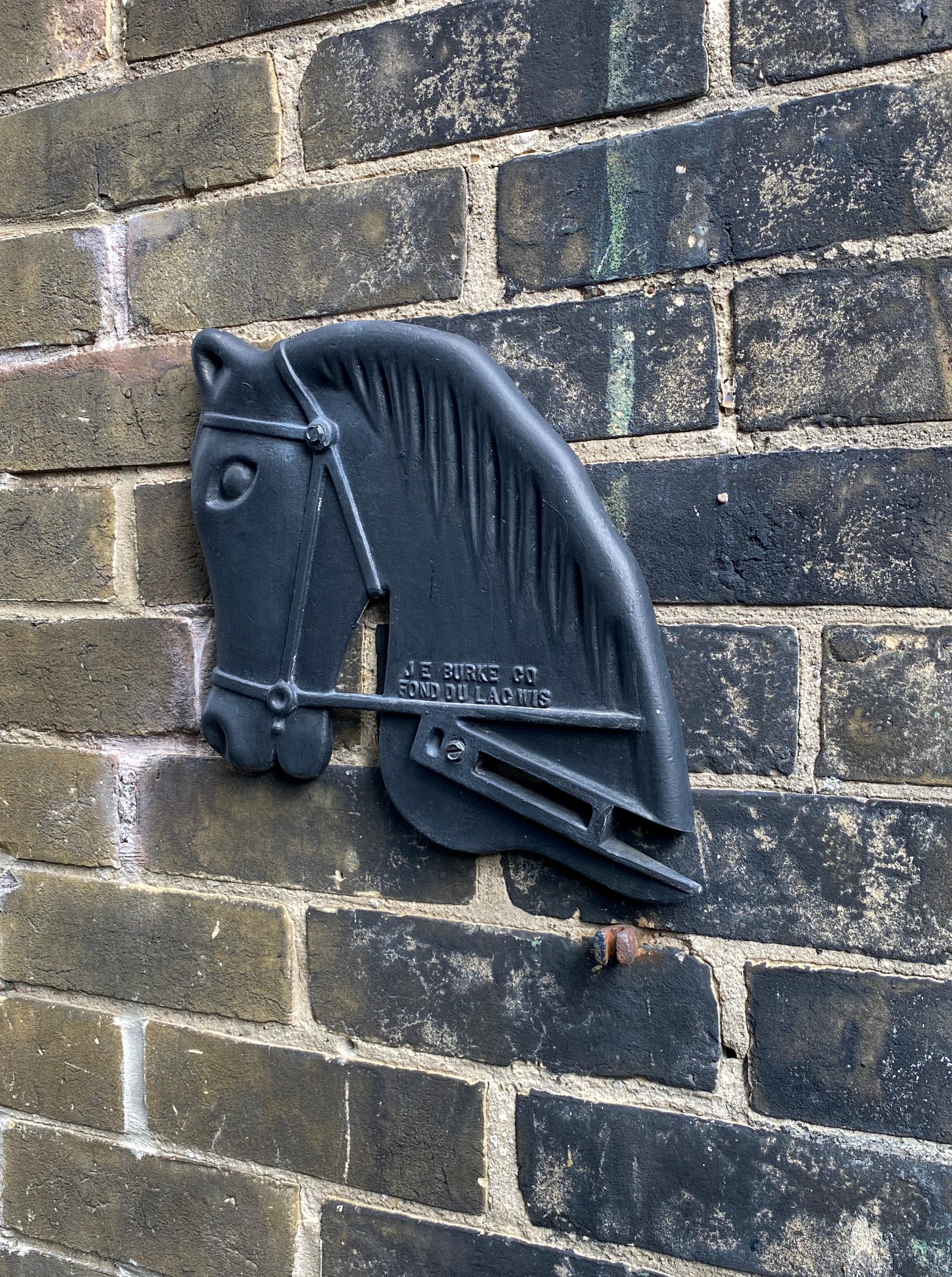 Brick wall with a relief sculpture plaque of a horse's head in profile.