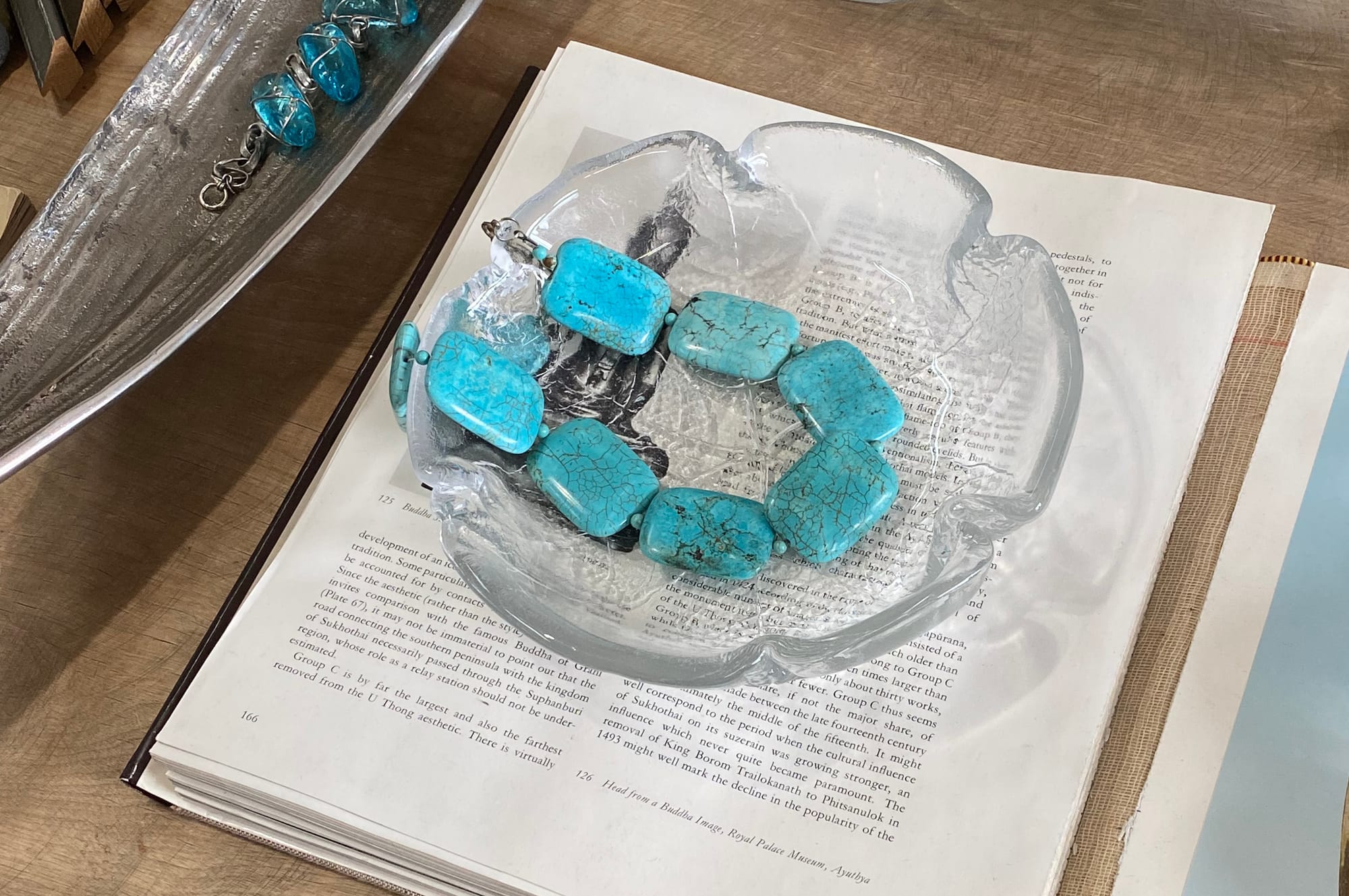 A strand of turquoise beads in a glass dish on top of an open book.