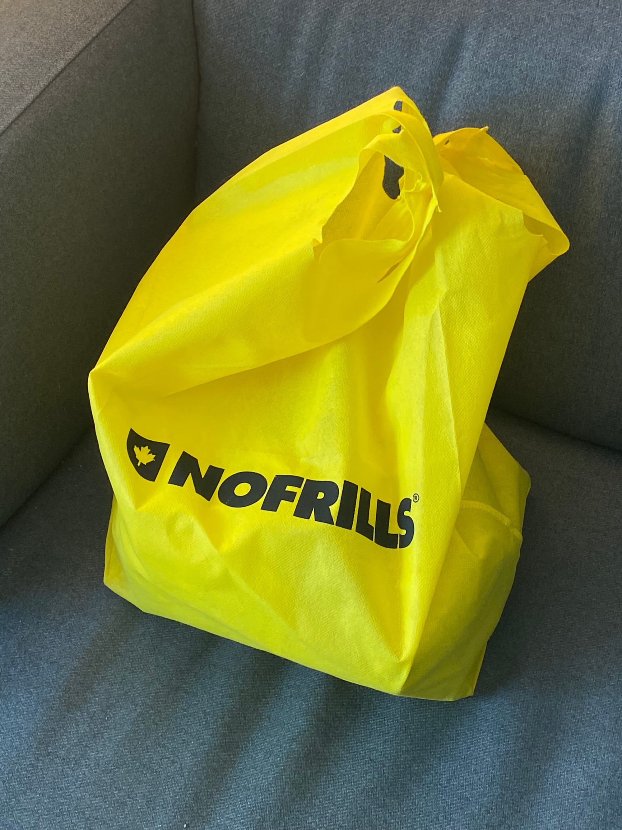 Yellow No Frills bag resting on a grey armchair.