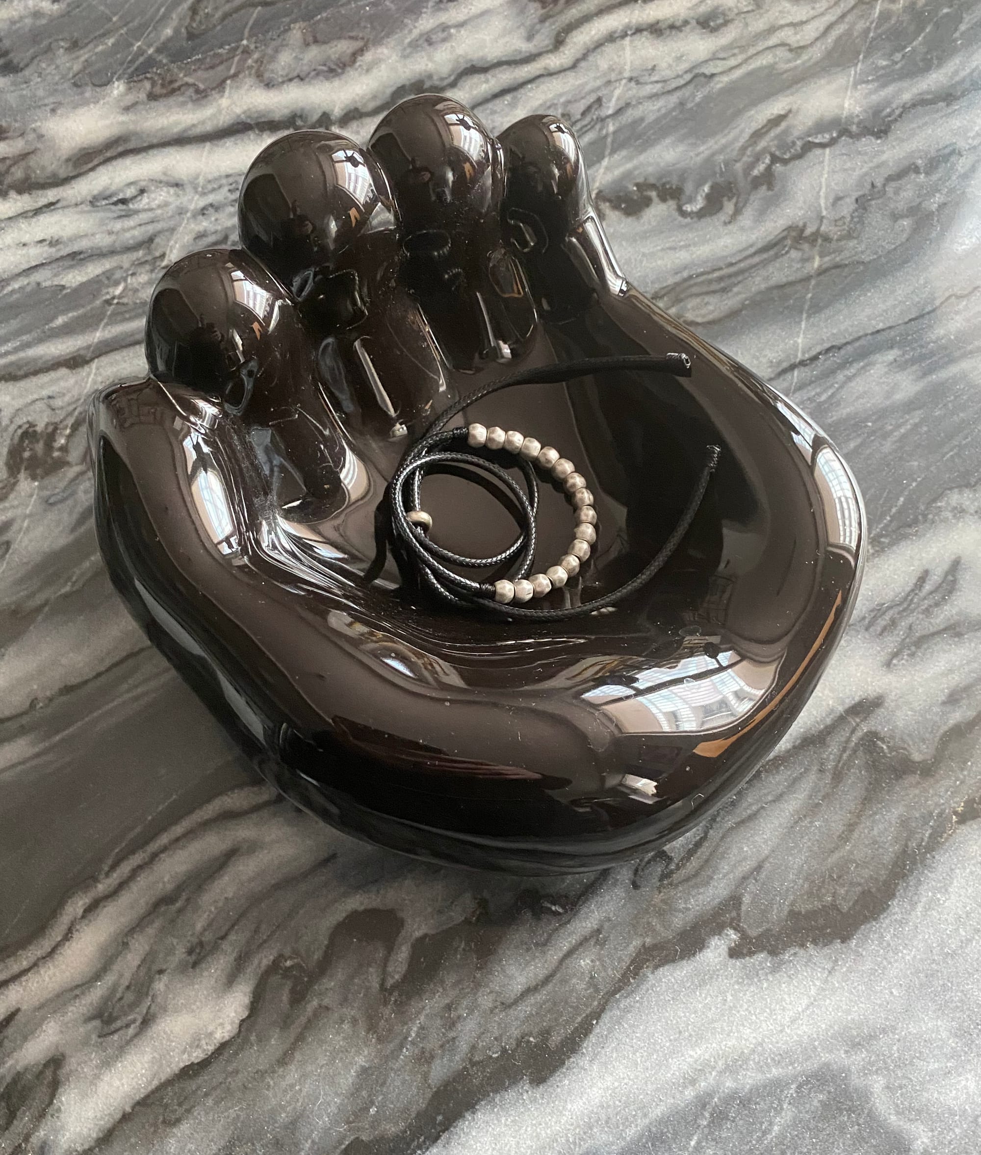 Glossy black ceramic hand with a necklace resting in its palm.