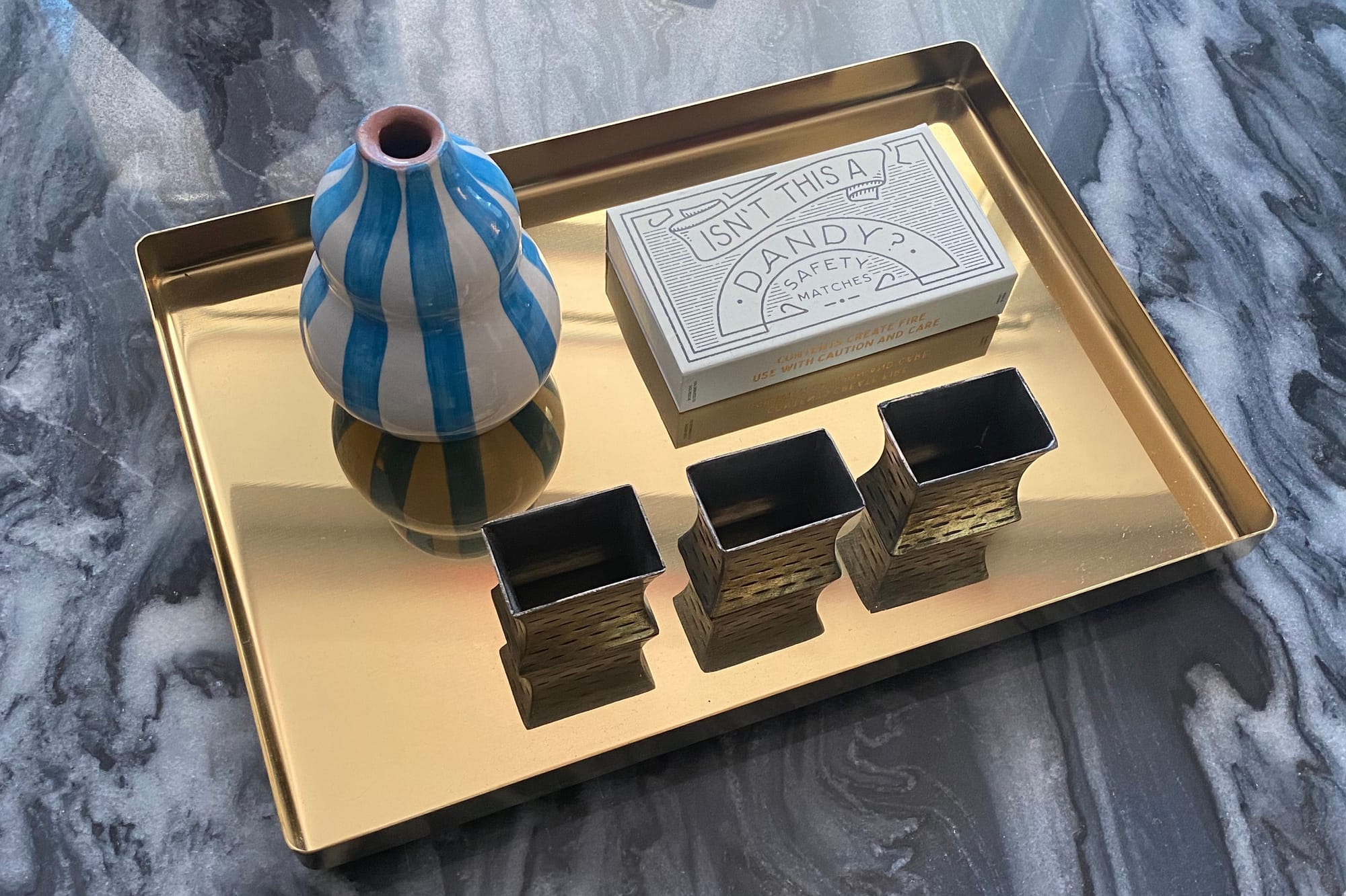 Brass-coloured tray displaying vase, napkins rings, and box of matches.