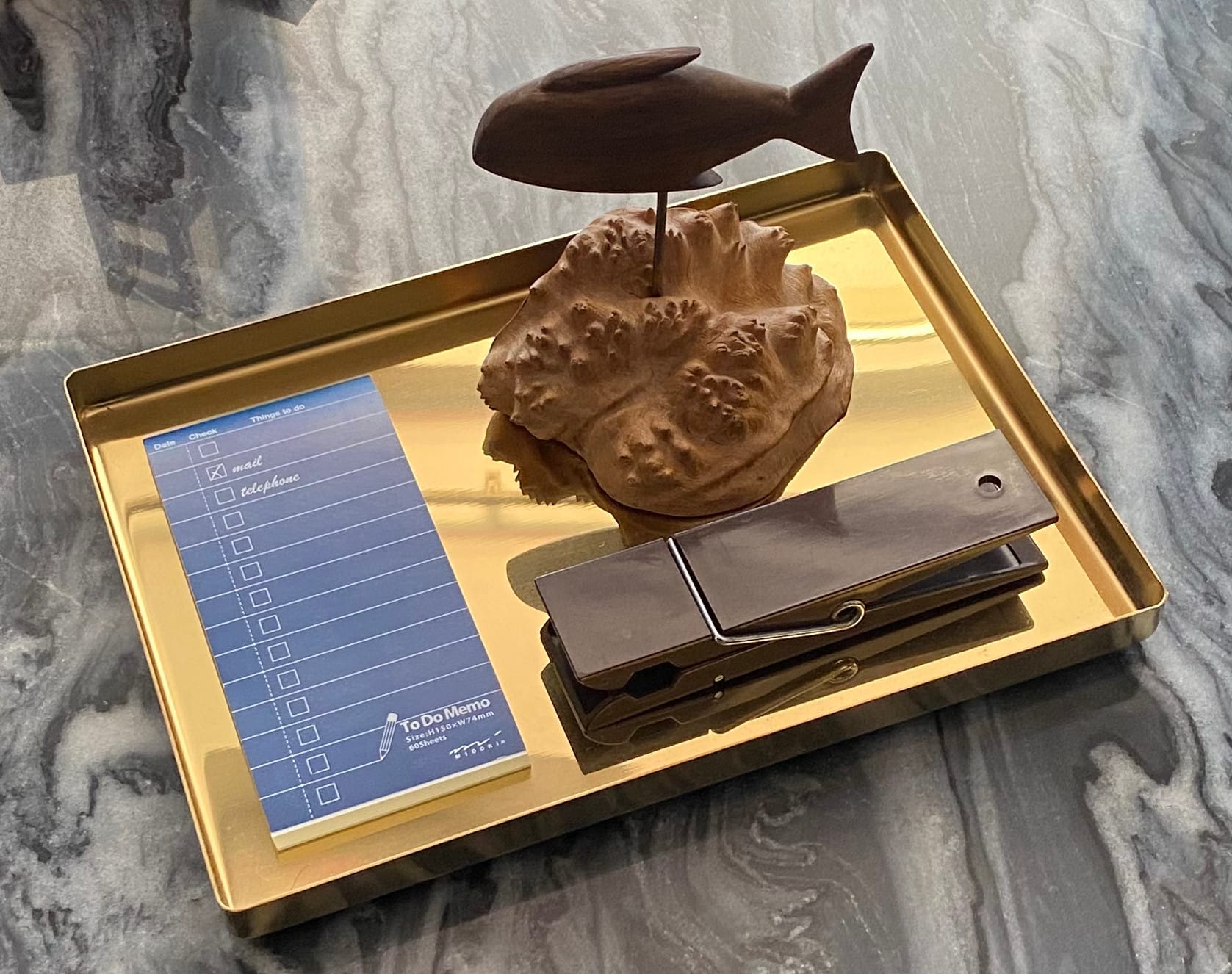 Brass-coloured tray displaying to-do memo booklet, fish sculpture, and large clothespin.