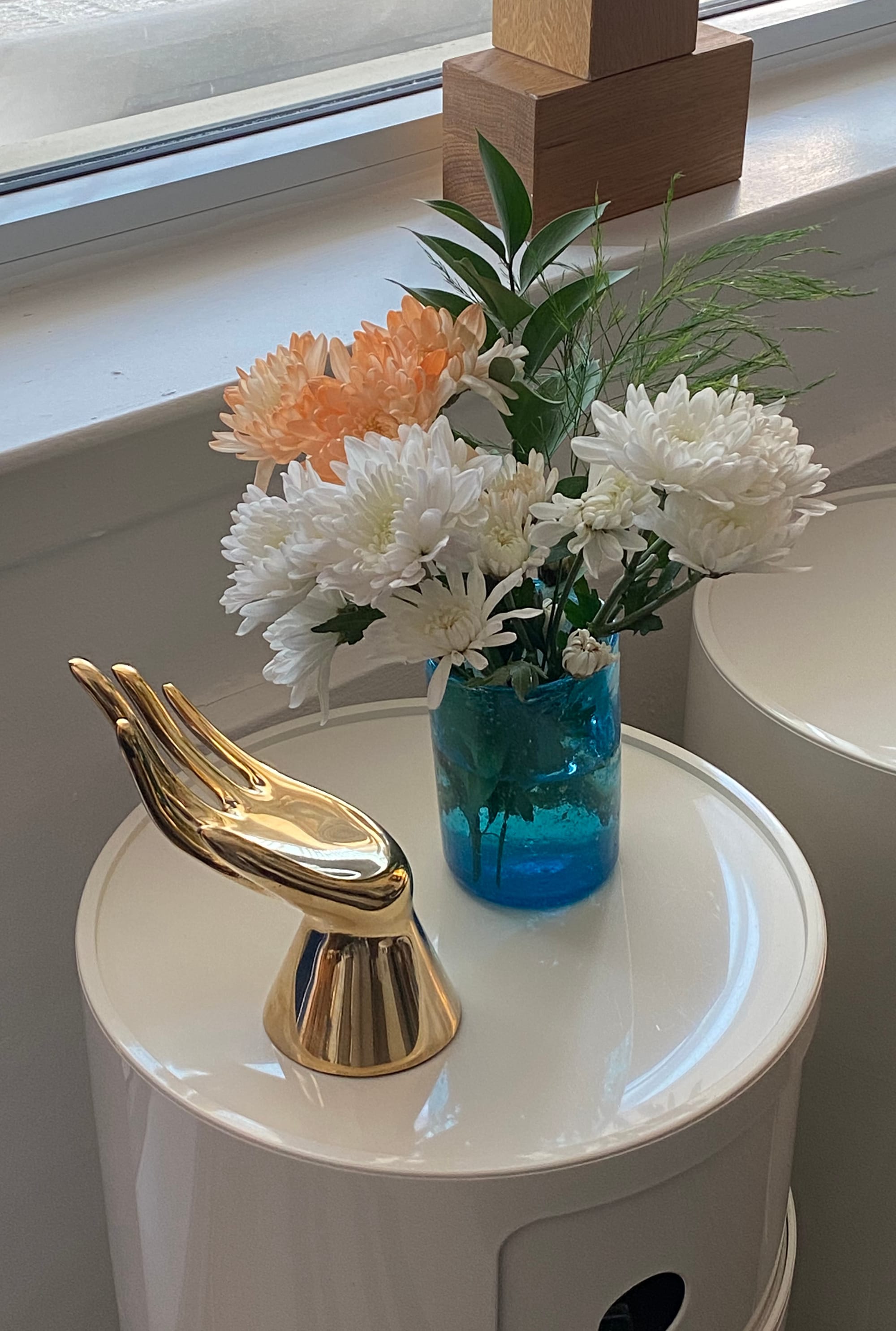 Turquoise blue drinking glass holding several flowers, with a brass sculpture of a hand nearby.