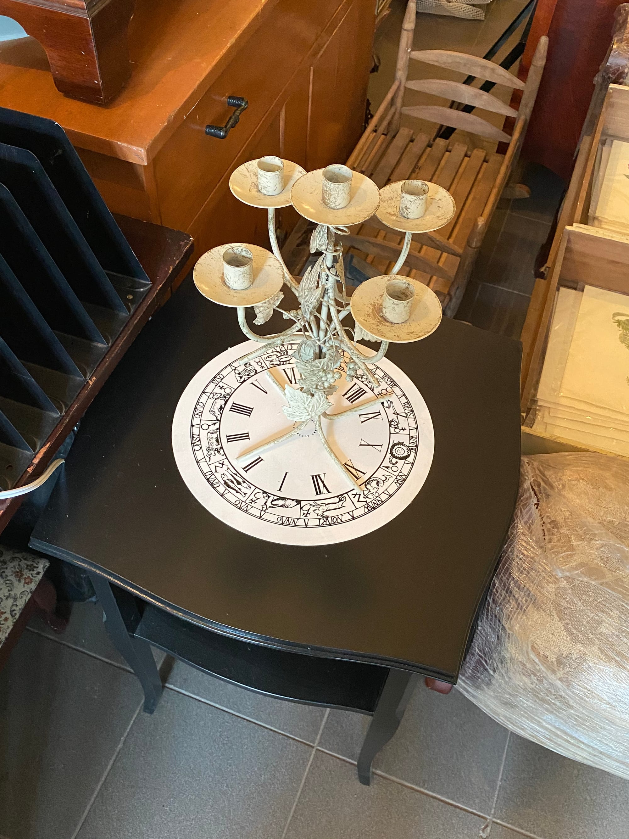 Clock face resting on a table top and supporting a metal candelabra.