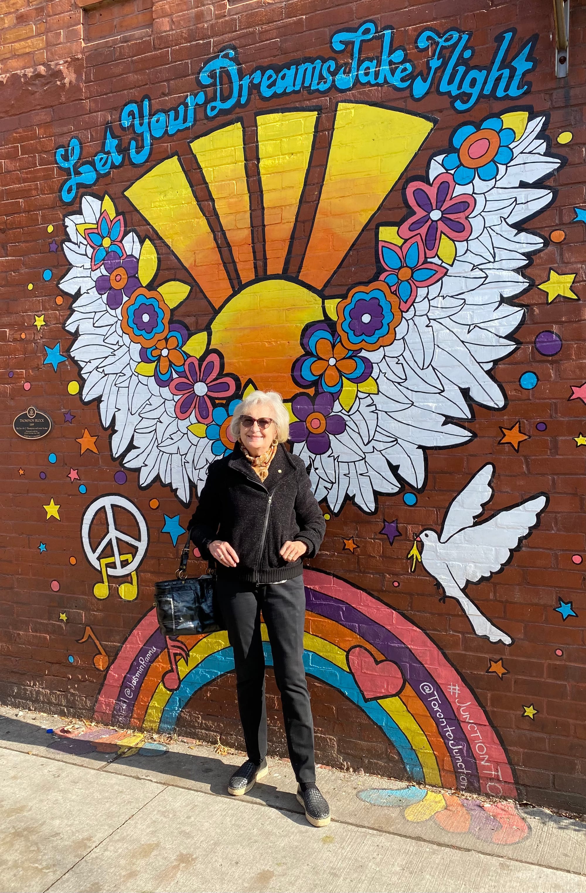 My Mom standing in front of a colourful wall mural.