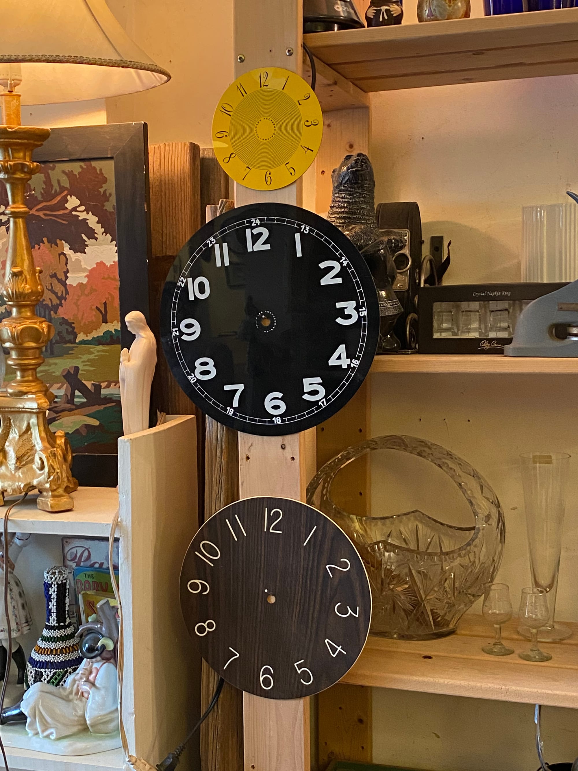 Three clock faces hanging on a wooden shelving unit, surrounded by other vintage objects
