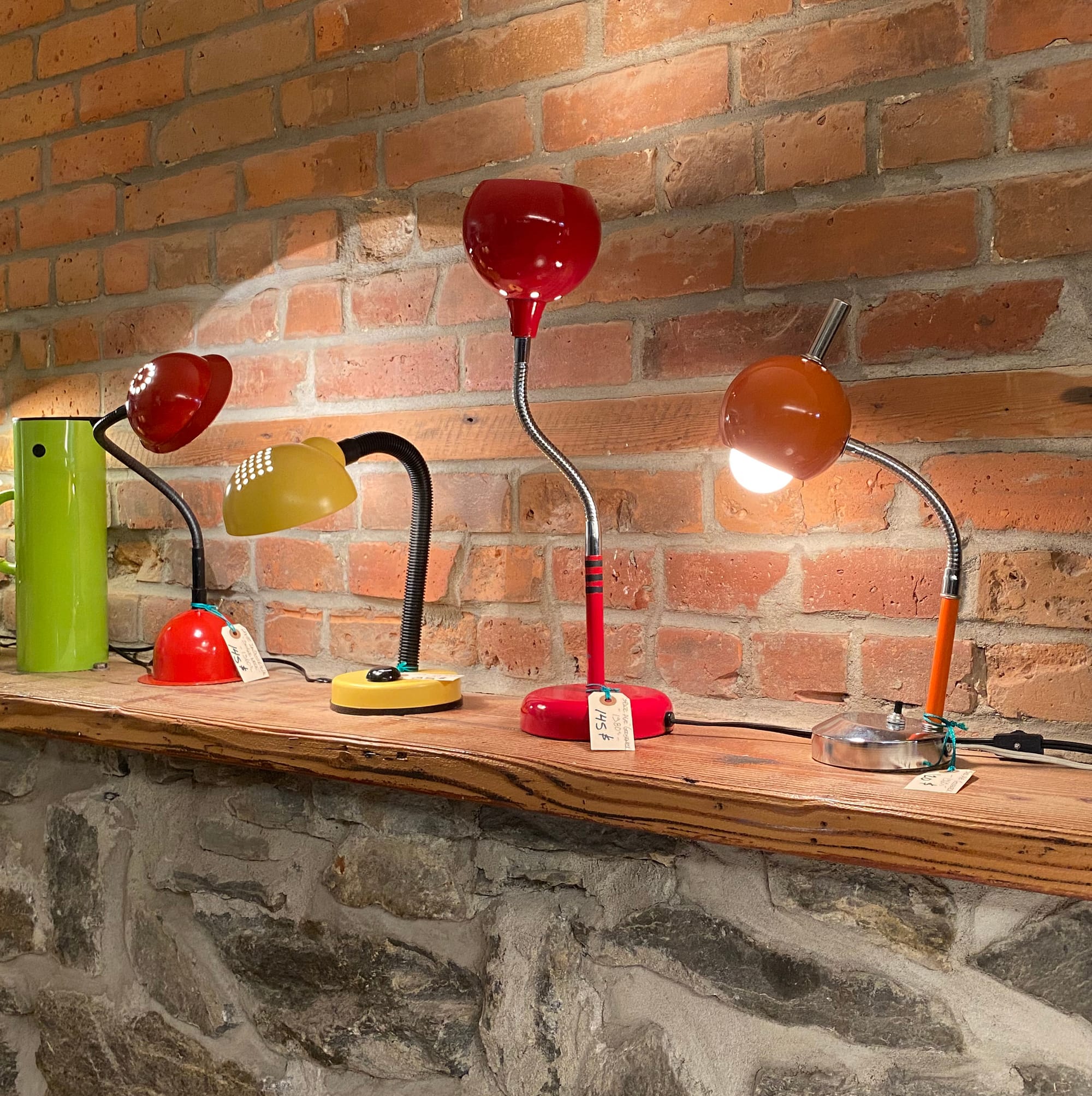 Four desk lamps on a shelf, each of them with a bendy neck.