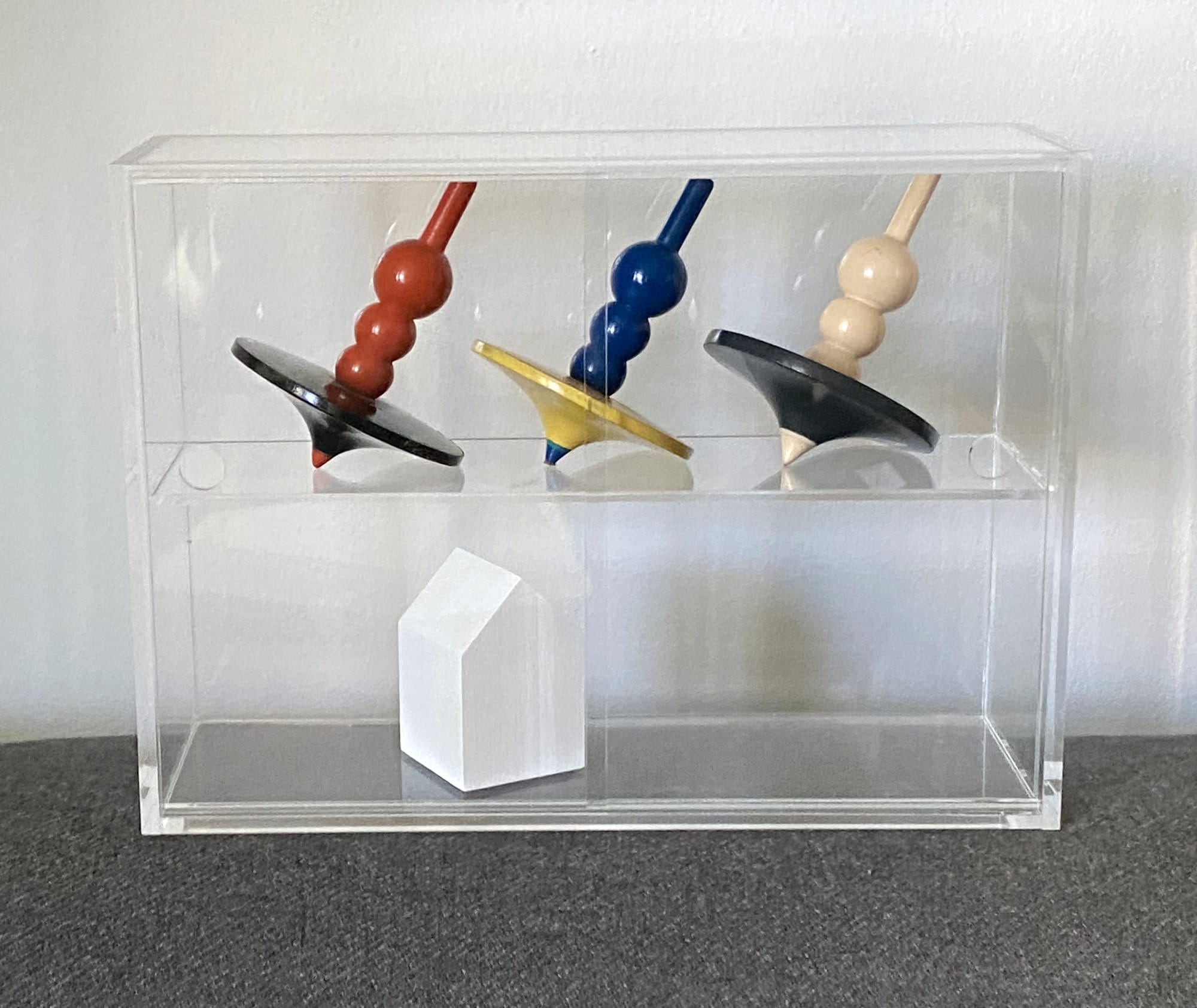 Three spinning tops in a small acrylic shelving device.