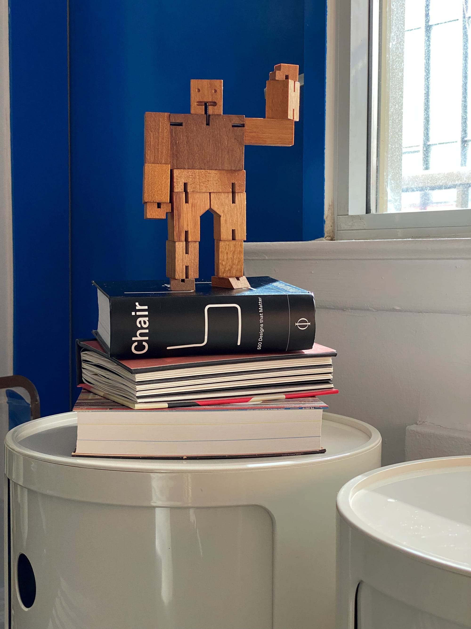 Another shot of the Cubebot, this time standing on a stack of books, one hand upraised in a wave.