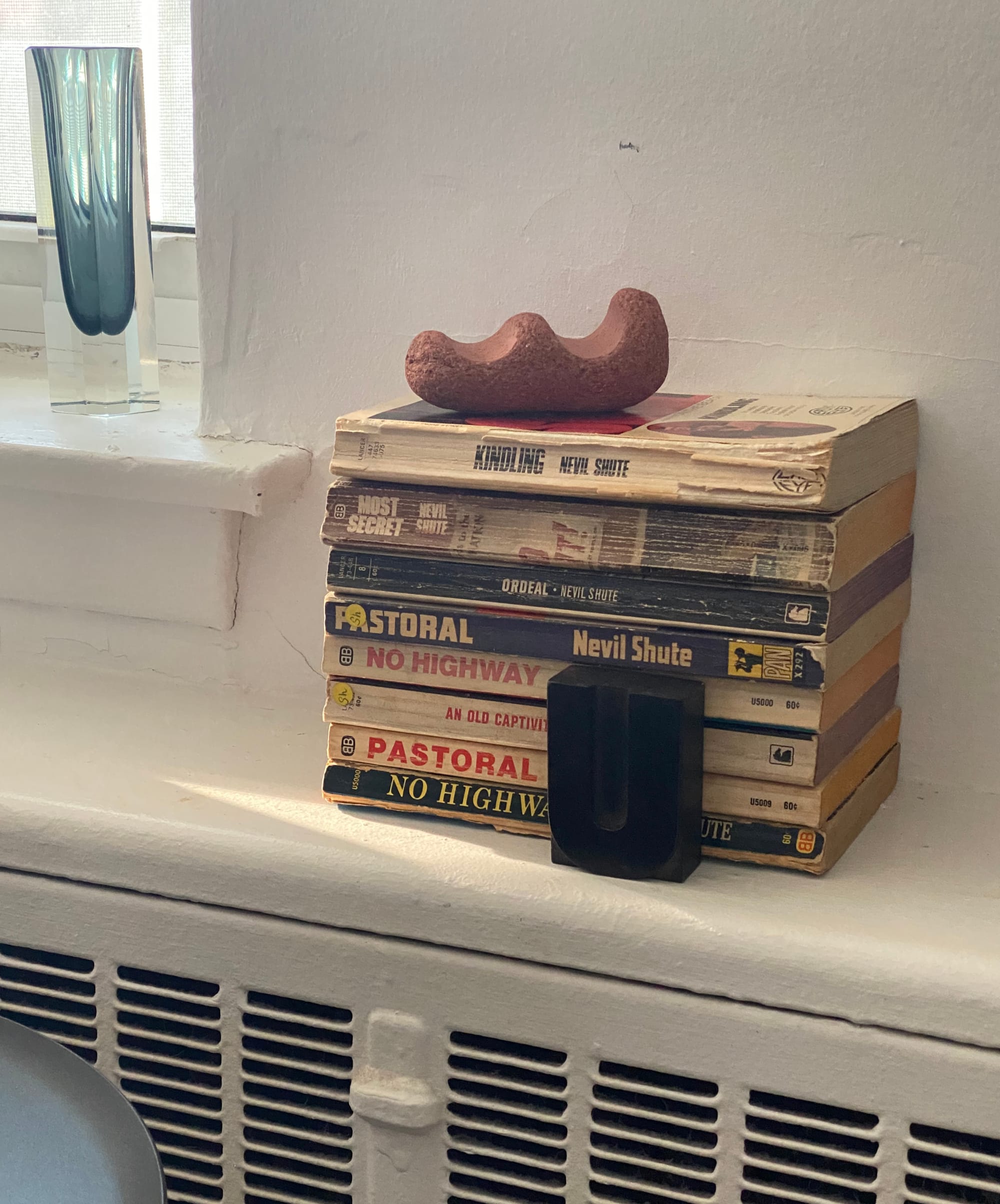 Red clay object on top of a stack of paperbacks.
