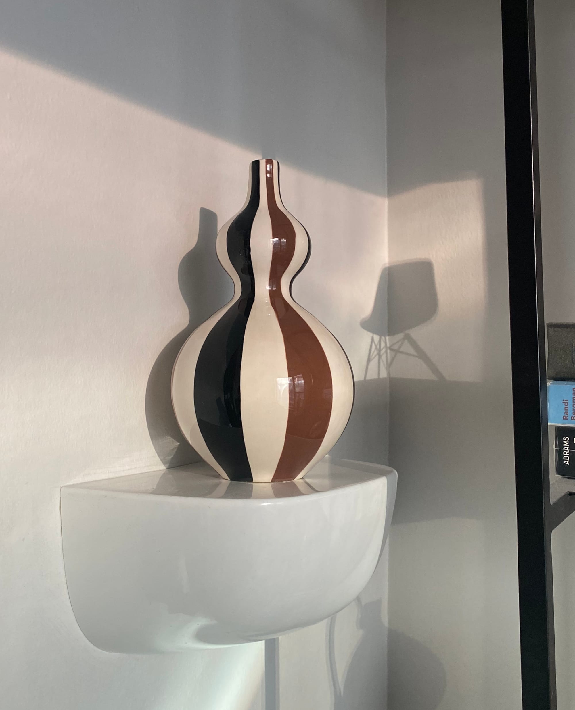 A patterned vase on a small acrylic wall shelf.