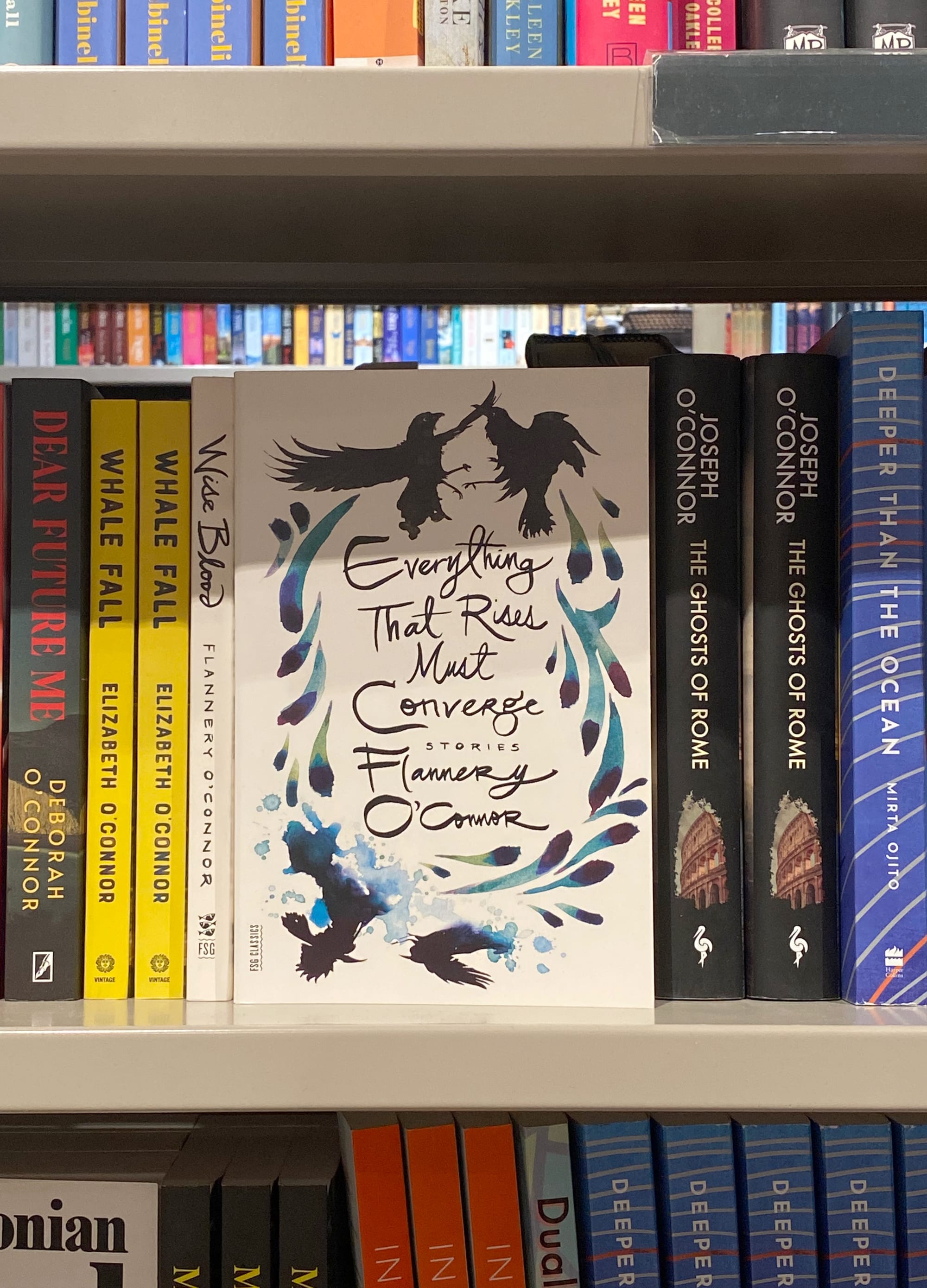 A book of Flannery O'Connor stories facing out on a crowded bookshelf.