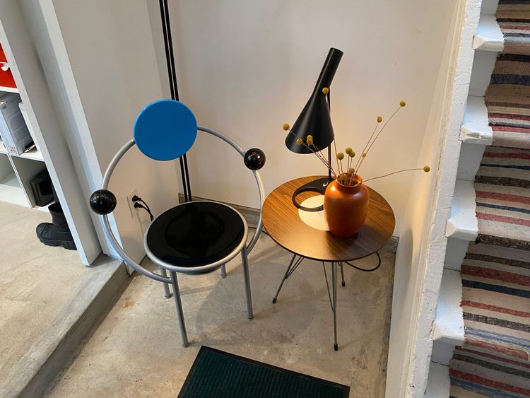 A cozy entryway with a modern chair, side table, table lamp and vase with dried flowers.