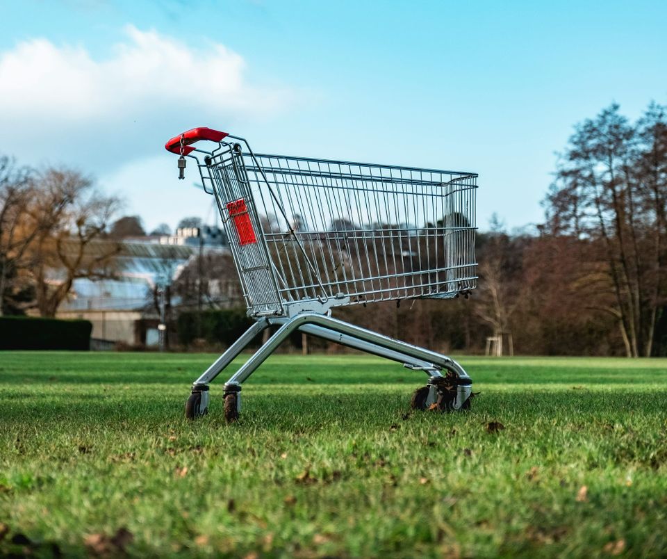 An empty shopping cart in a grassy field.