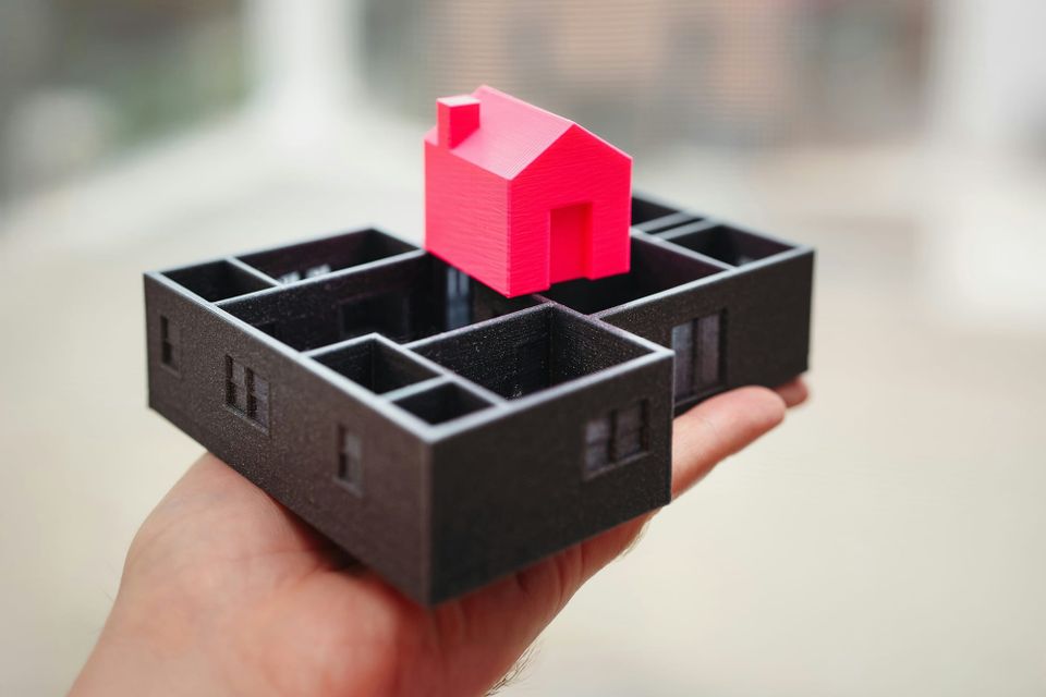 Hand holding a small model of the first floor of a house with a smaller toy house resting on top.