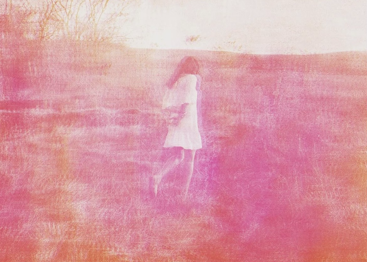 A person in a white dress walks through a field, enveloped in a pink haze. The soft, dreamy atmosphere evokes a sense of tranquility and nostalgia.