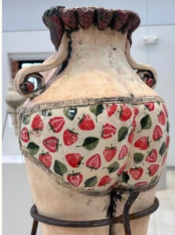 A ceramic vase with curved handles, featuring a whimsical design of strawberry-patterned shorts on its lower half, creating a playful and humorous tone.