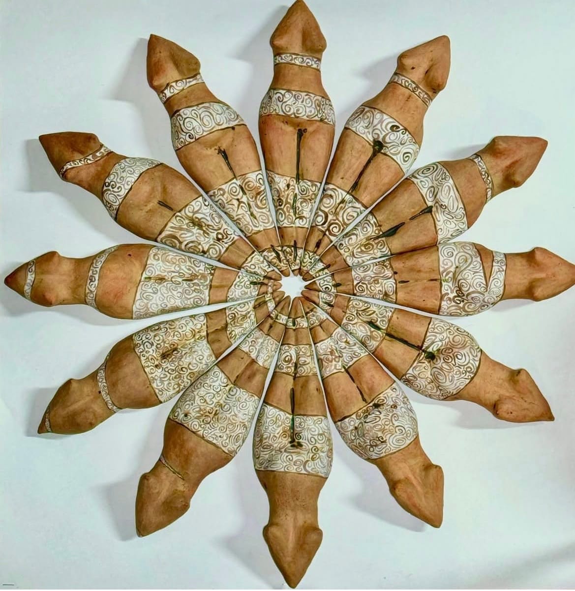 Ceramic objects arranged in a circular pattern resembling a sunburst. Each piece is a torso featuring intricate white carvings, creating a harmonious and symmetrical design.