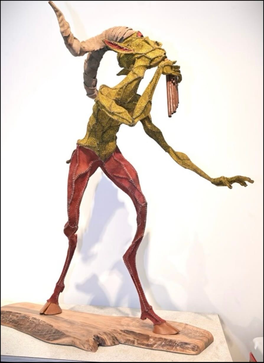 A humanoid sculpture of a goat, the creature stands on two hooved feet and plays a pan flute.