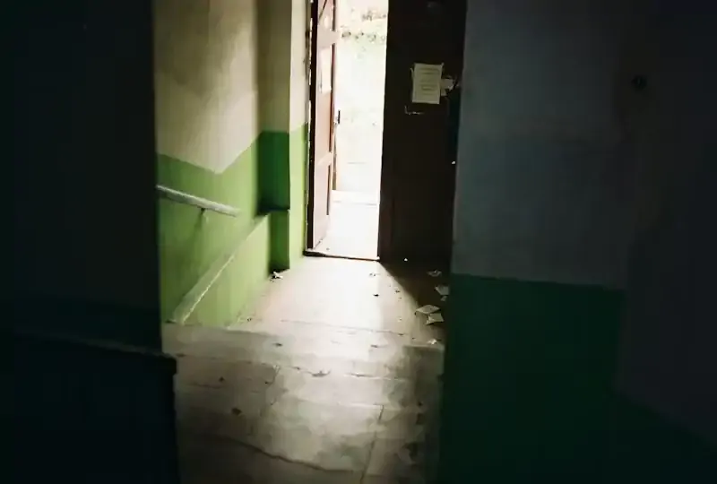 Image of a doorway to the outside at the bottom of a dark stairwell. The photo has an air of desolation.