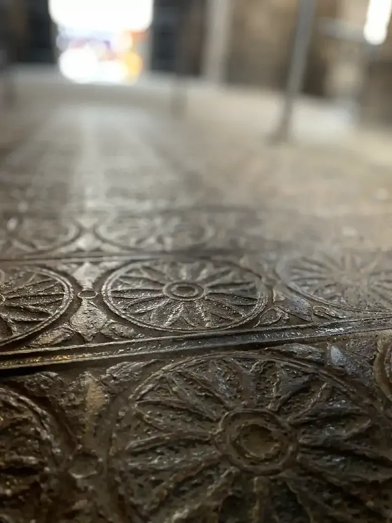 Close-up of a textured floor with circular floral patterns in a dimly lit corridor. The background is blurred, adding depth and a historic ambiance.