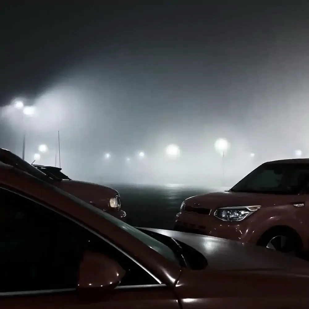 Cars parked in a thick fog, partially obscured, creating a mysterious atmosphere. 