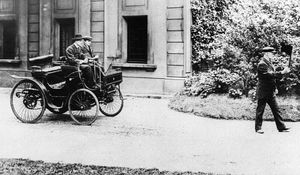 Charles Rolls in an 1896 Peugeot, with a man walking ahead carrying a warning flag. Photo: unknown, c. 1896, via Wikimedia Commons (public domain).