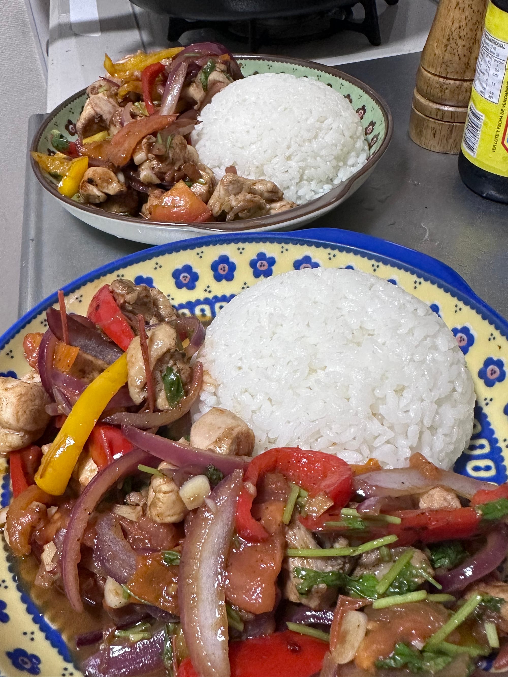 A dish of stirfry, chicken, red onions, peppers, chili, tomato, topped with cilantro