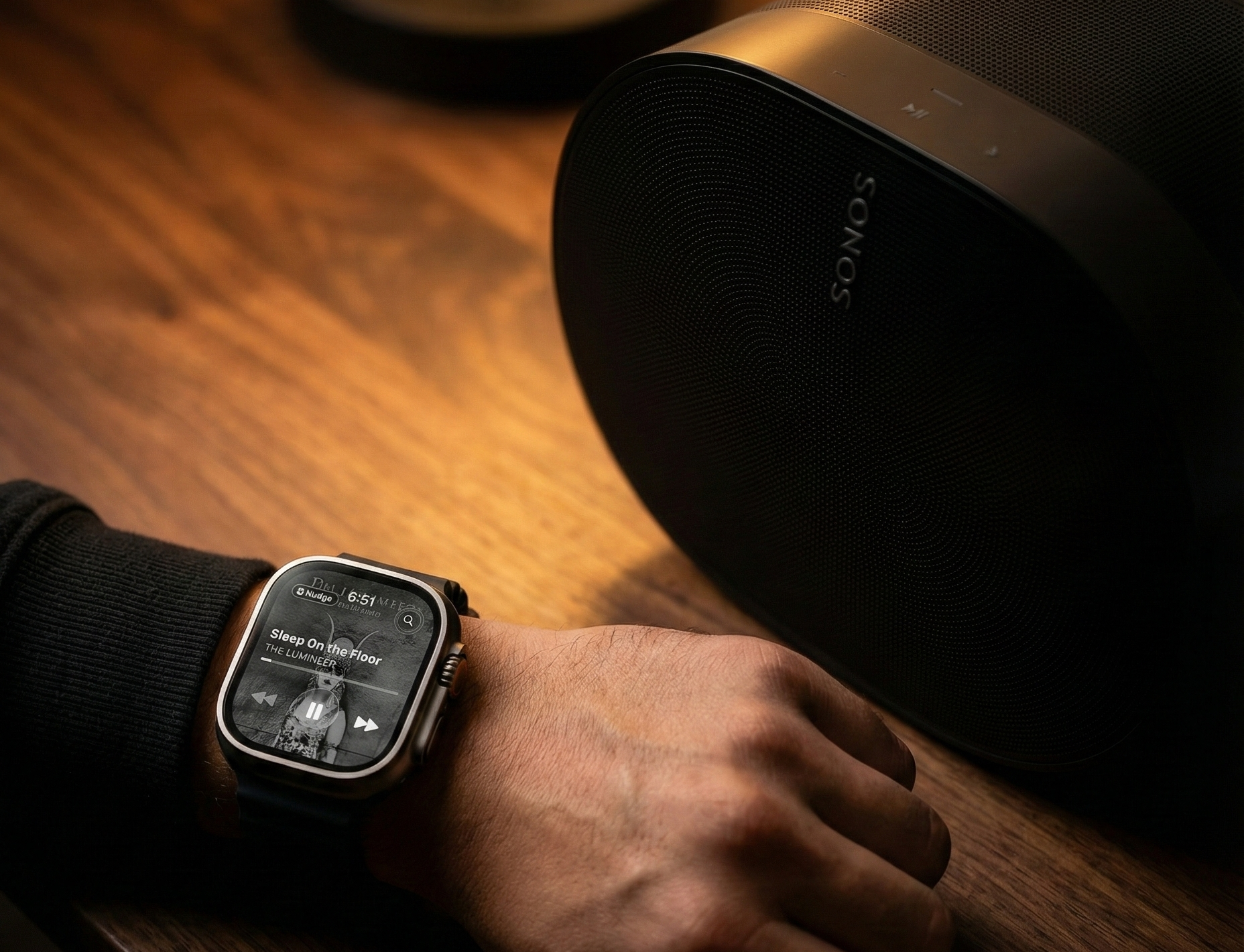 An Apple Watch showing Nudge playback controls beside a Sonos speaker