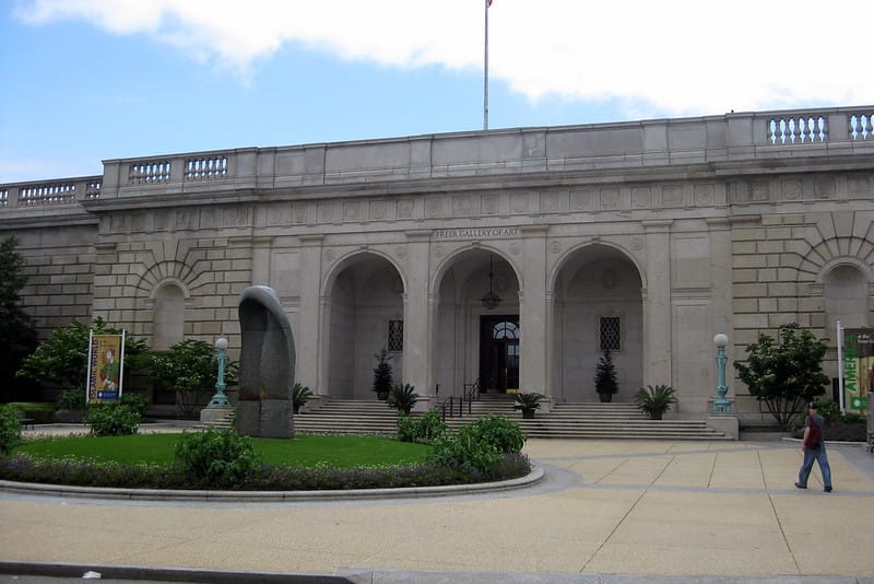 The exterior of a gray-ish colored museum with a green space in front.