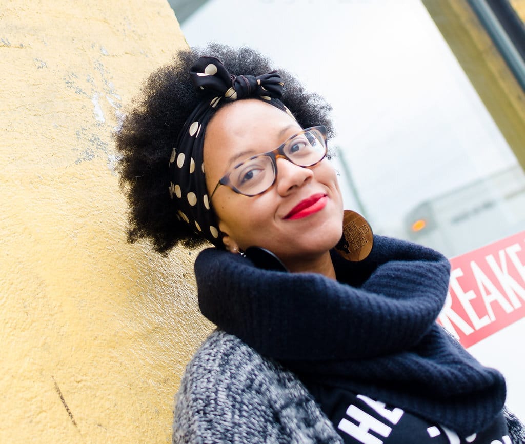 Team member Christina Sturdivant Sani, a Black woman, standing outside a yellow wall. 