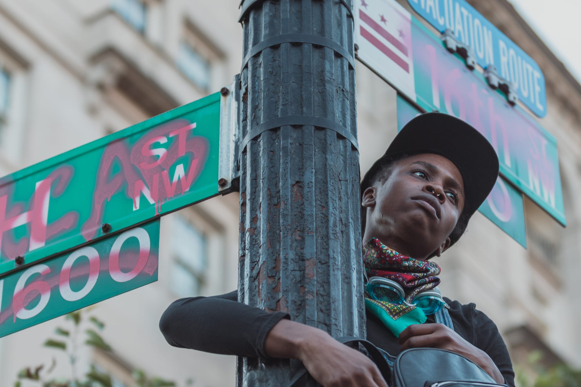 A black person hugs a pole of a street signs at the 16th and H St intersections. 
