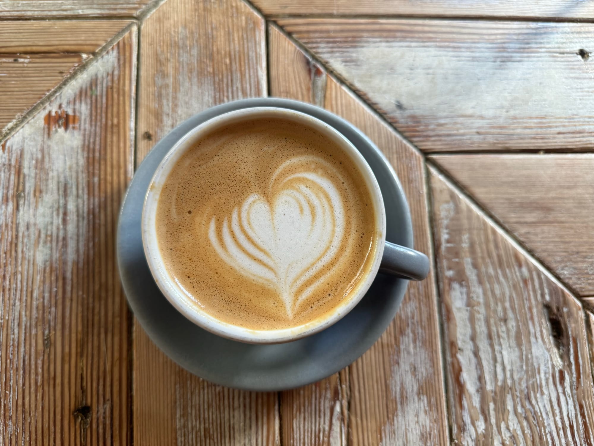 A latte with a heart of foam on top, resting on a wooden table. 