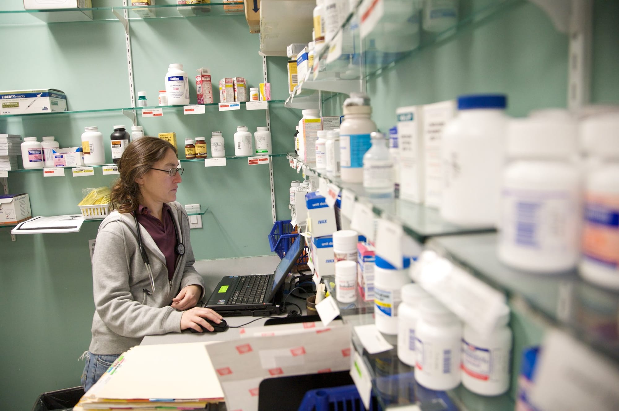 A clinic worker sits at a computer in a room filled with bottles of medication at Bread for the City.