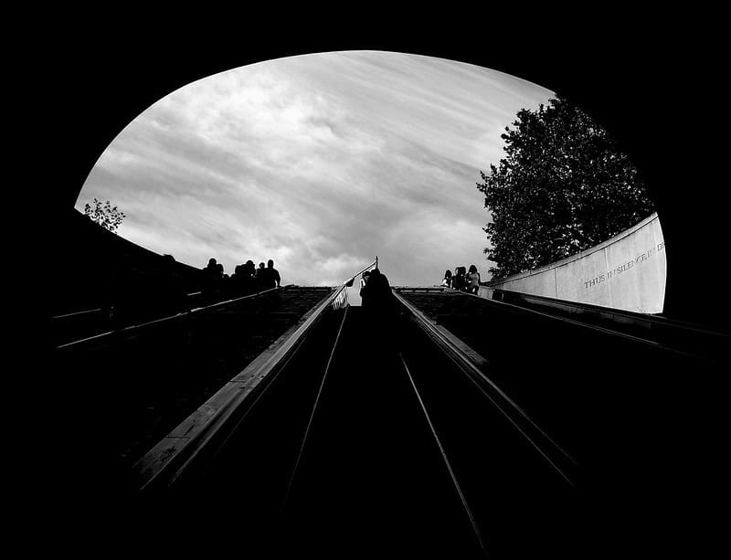 A black and white image an escalator leading out of a metro station. 